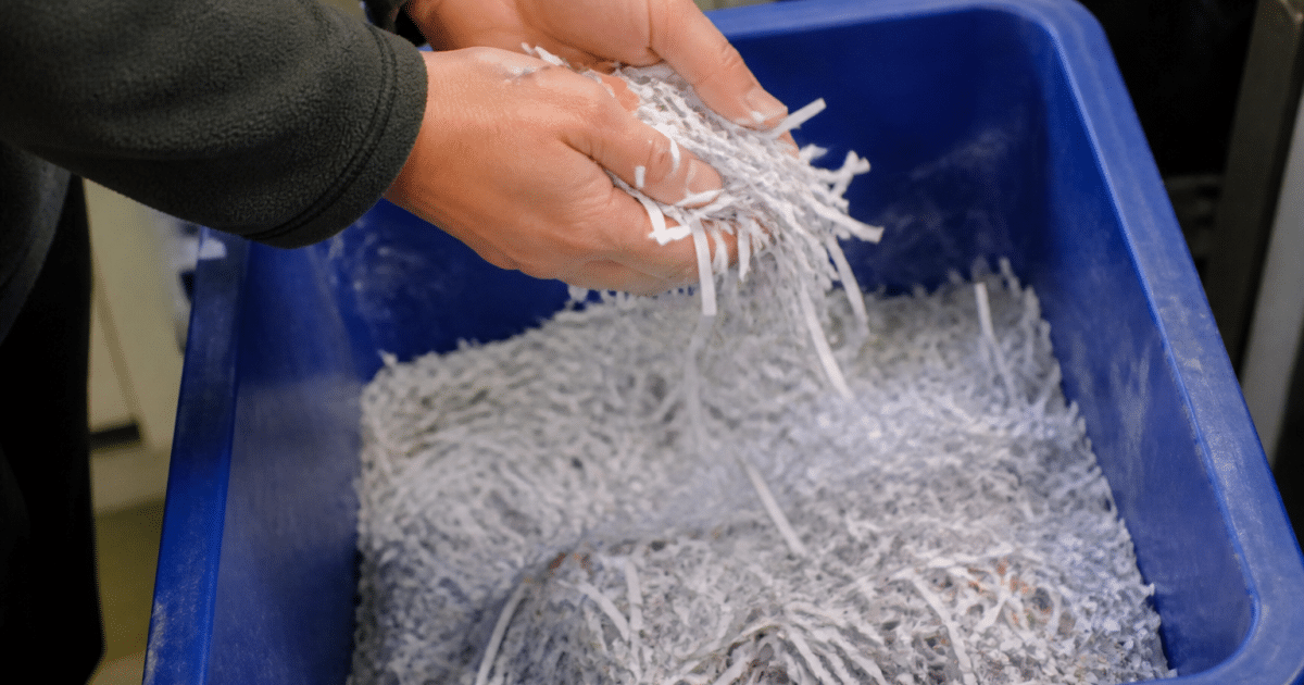 Mains versant papier déchiqueté dans bac recyclage bleu
