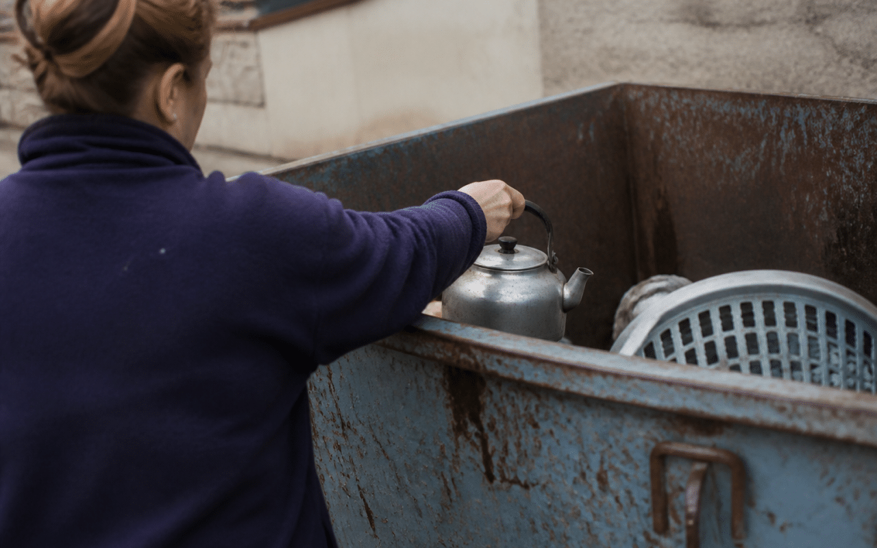Personne deposant une vieille bouilloire metallique dans benne.