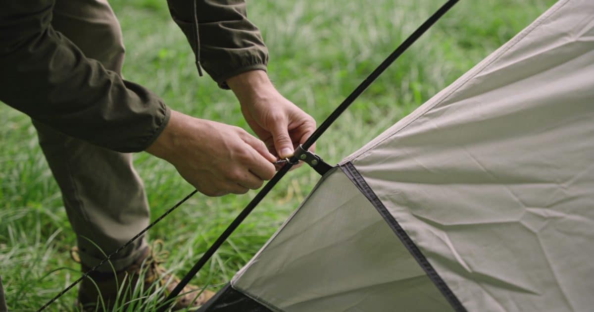Personne installant une tente sur terrain herbeux verdoyant.