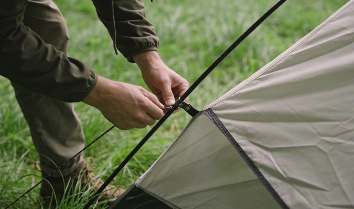 Personne installant une tente sur terrain herbeux verdoyant.