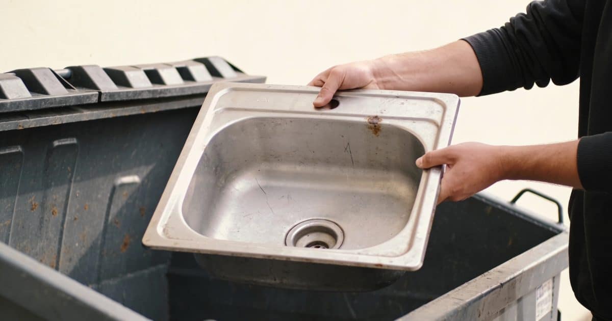 Personne tenant un vieux lavabo metallique au-dessus d'une benne.