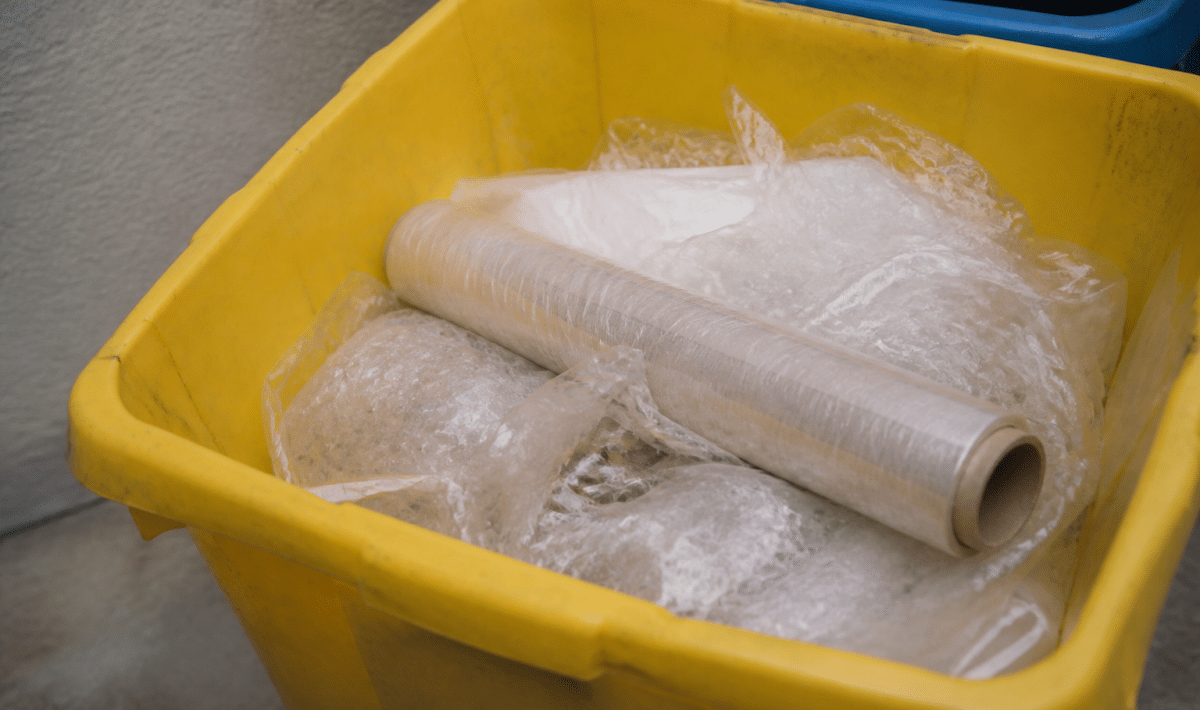 Rouleau de film plastique transparent jeté dans bac recyclage.